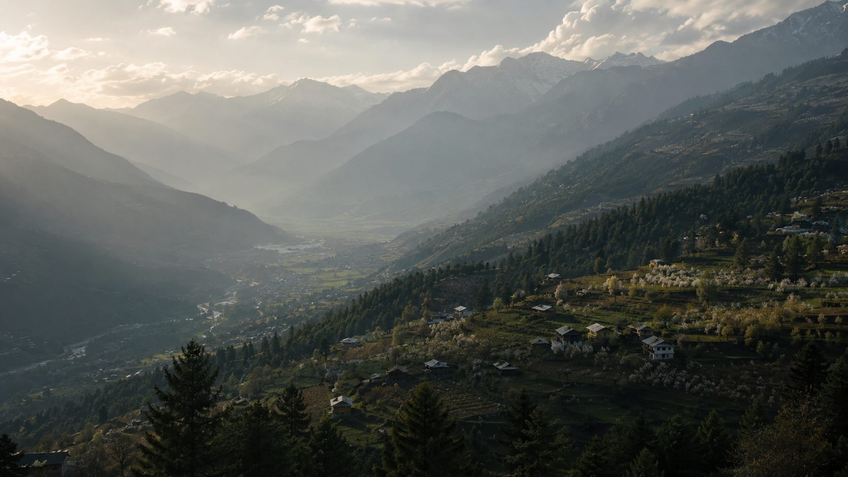 The valley at first light — a river threading between villages and orchards in bloom, mist and snow up the ridge.