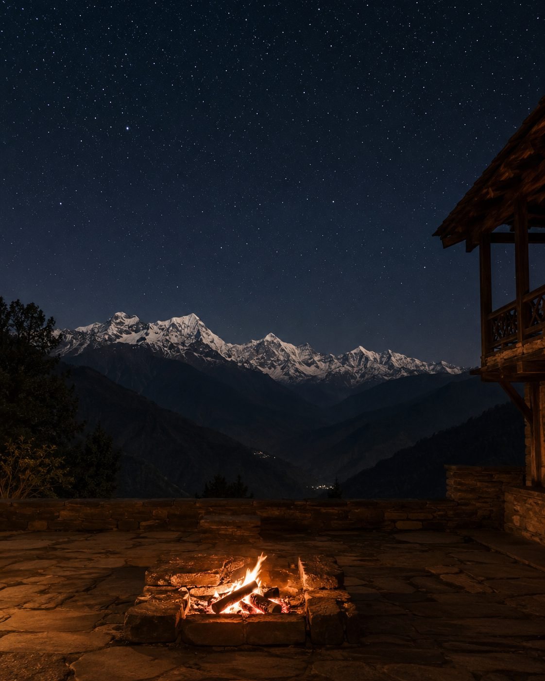 A stone fire pit burning on a terrace at night — the snow-lit range across the valley, and a sky full of stars above.