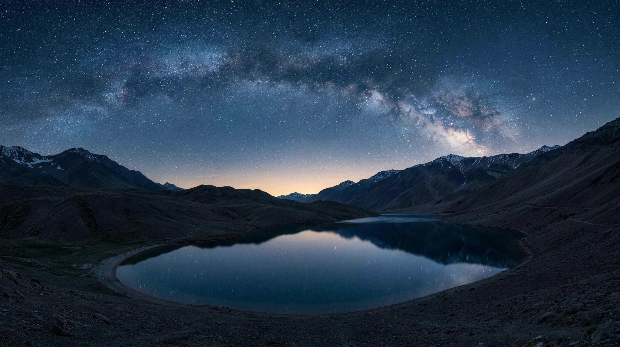 Camp tents below the night sky near Chandratal, one window glowing warm against the dark ridge and the Milky Way.