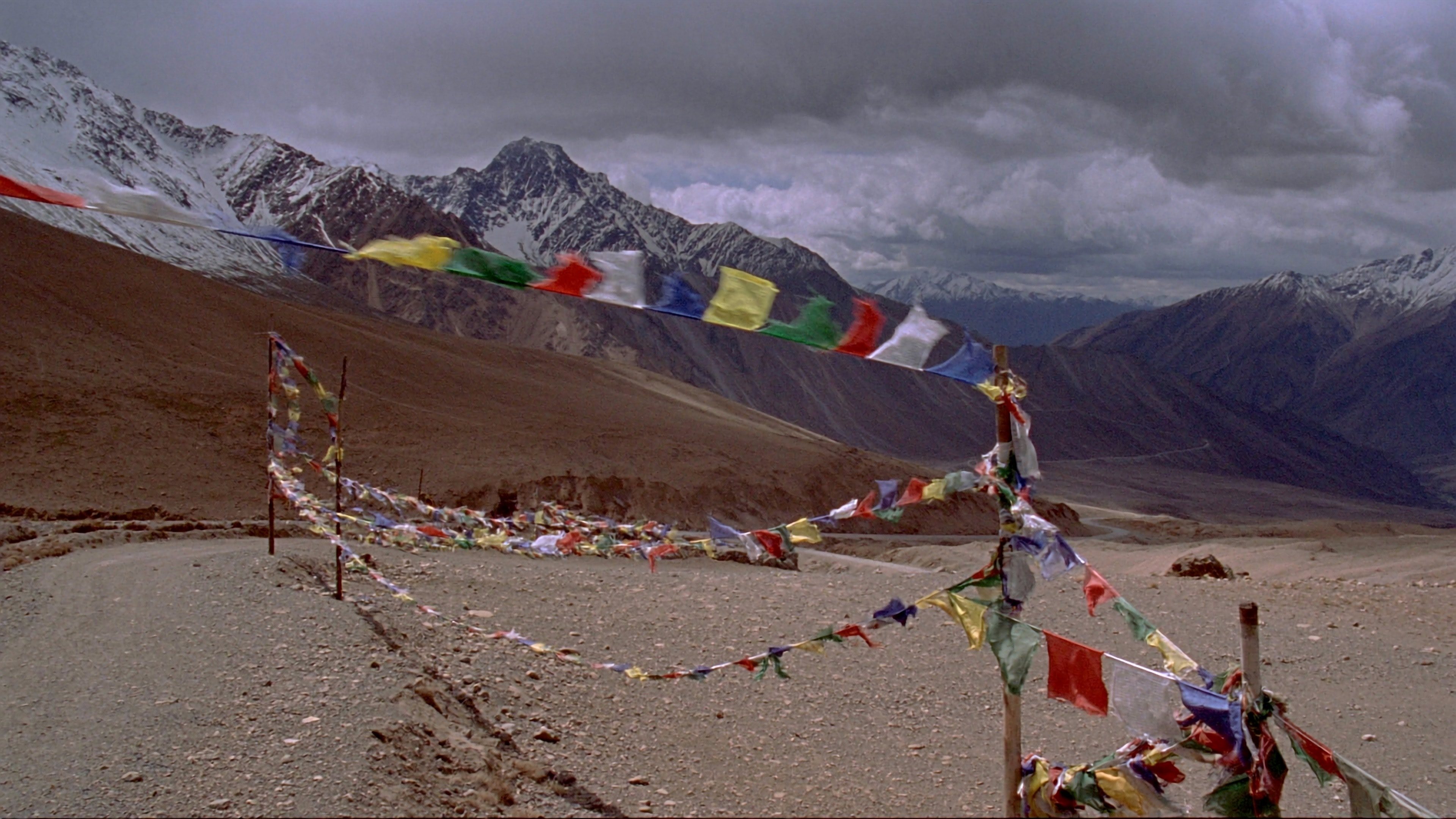 Prayer flags strung across Kunzum La, bare peaks and a wide cold sky beyond the pass.